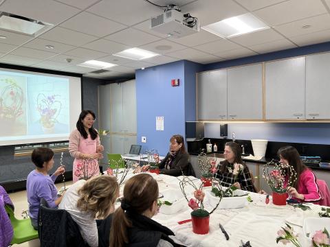 Instructor holds flower in front of table with sitting participants.